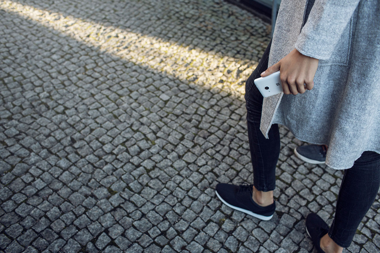 A woman walking on the street holding a Lumia 550