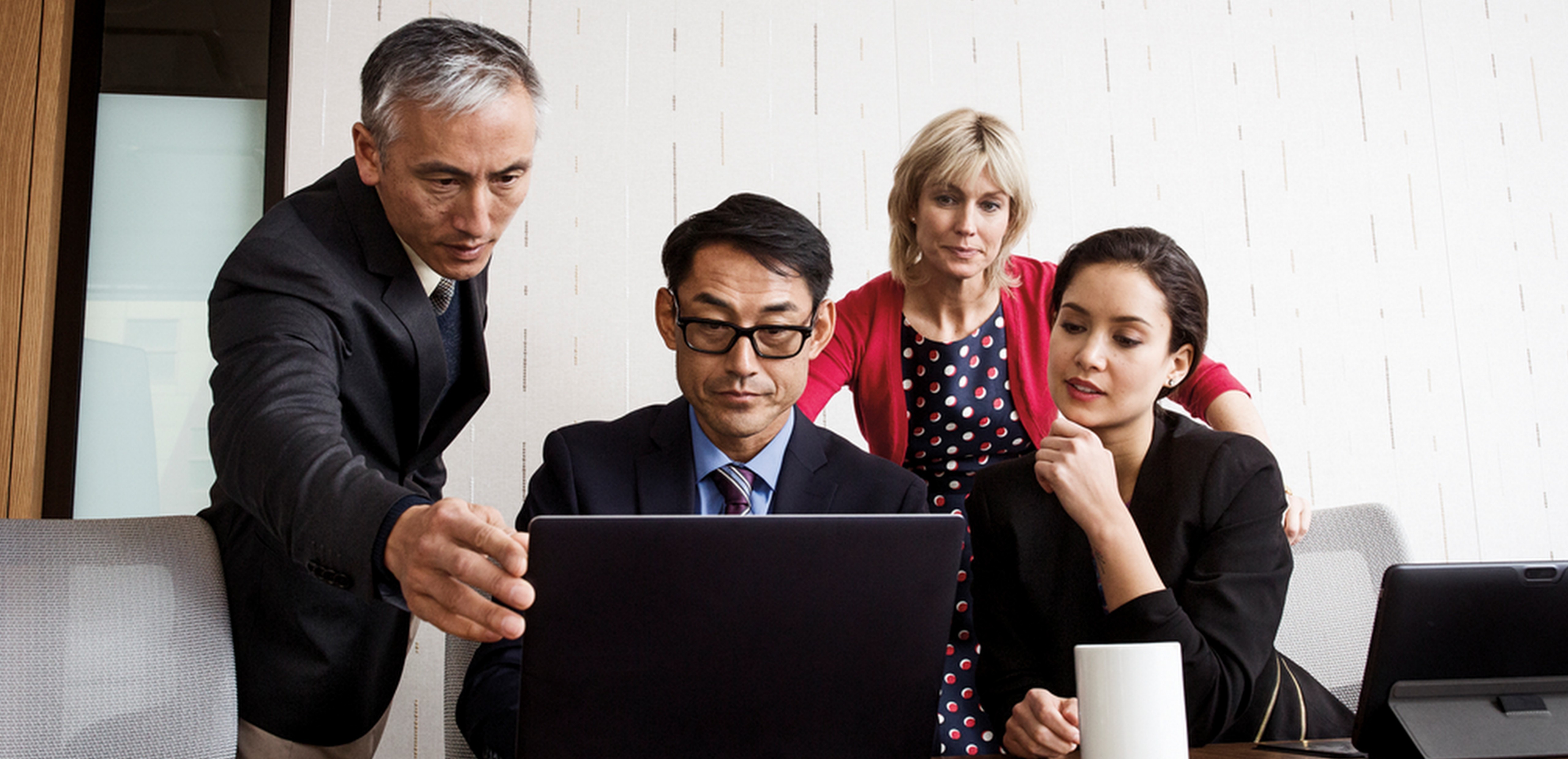 Two men and two women sitting around a conference table in an office environment looking at PC