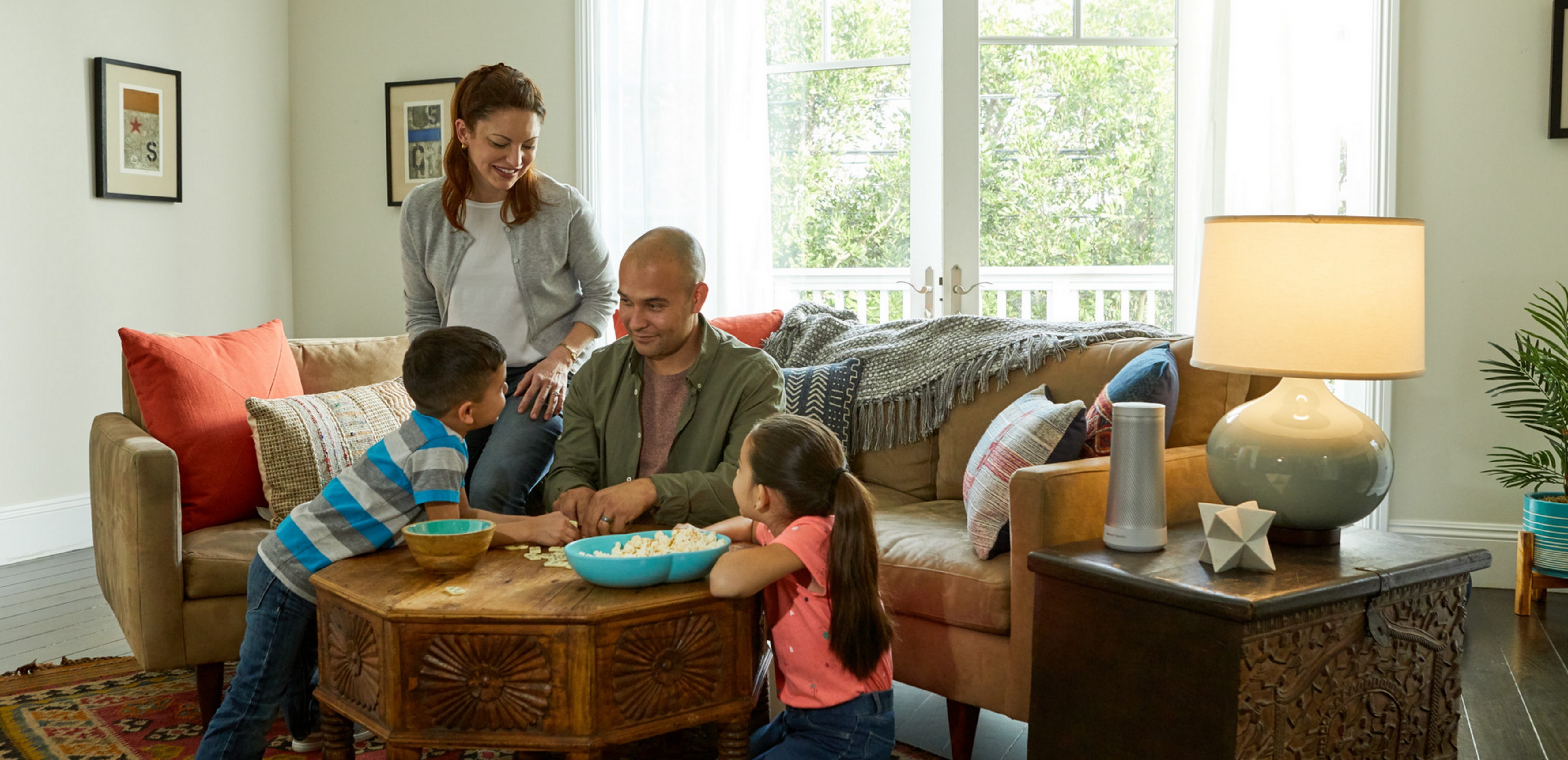 A family, two children, a mother and father sit around a table in a living room.
