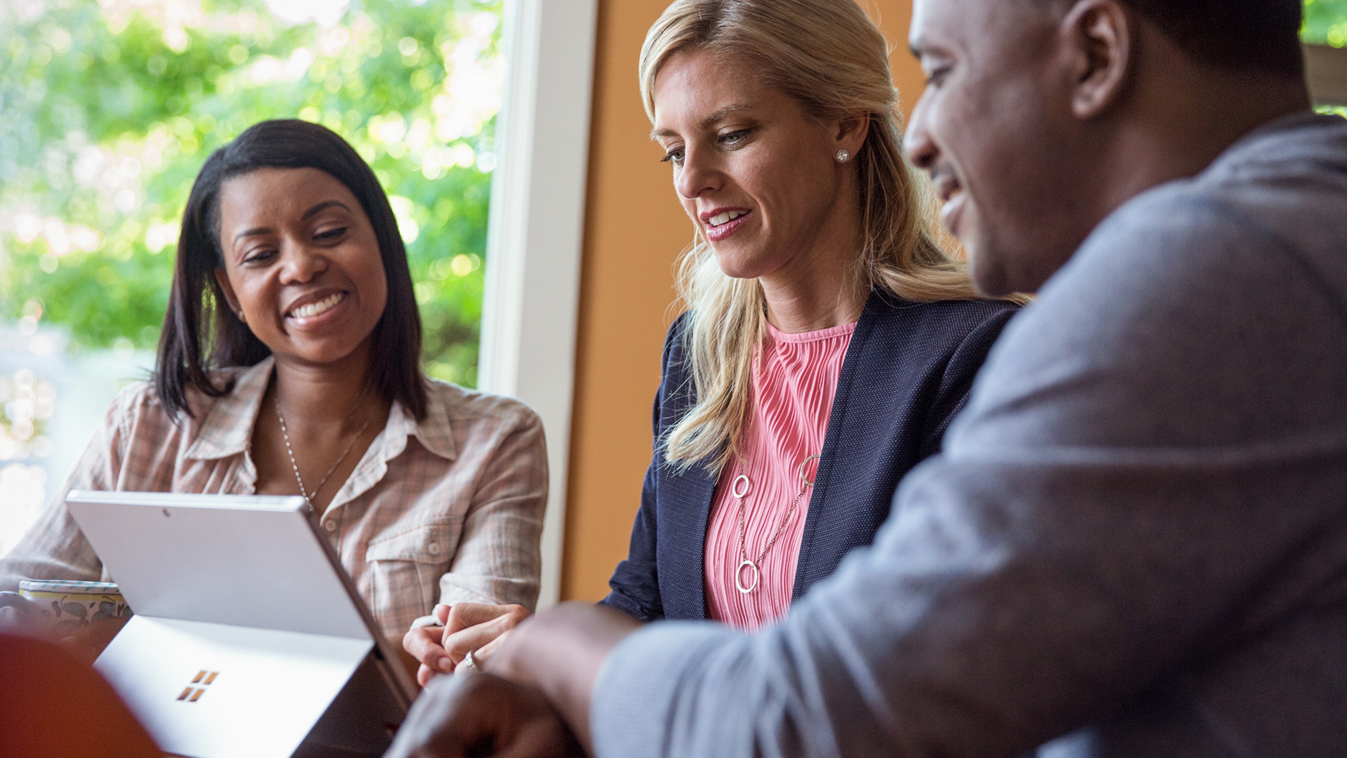 Three people sitting at a table looking at a Surface Pro.