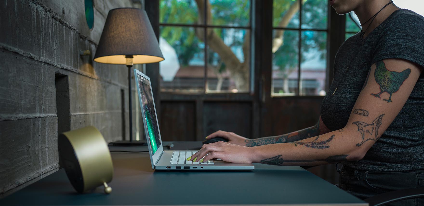 Person with a tattoo sitting at a desk working on a Razer Blade 15