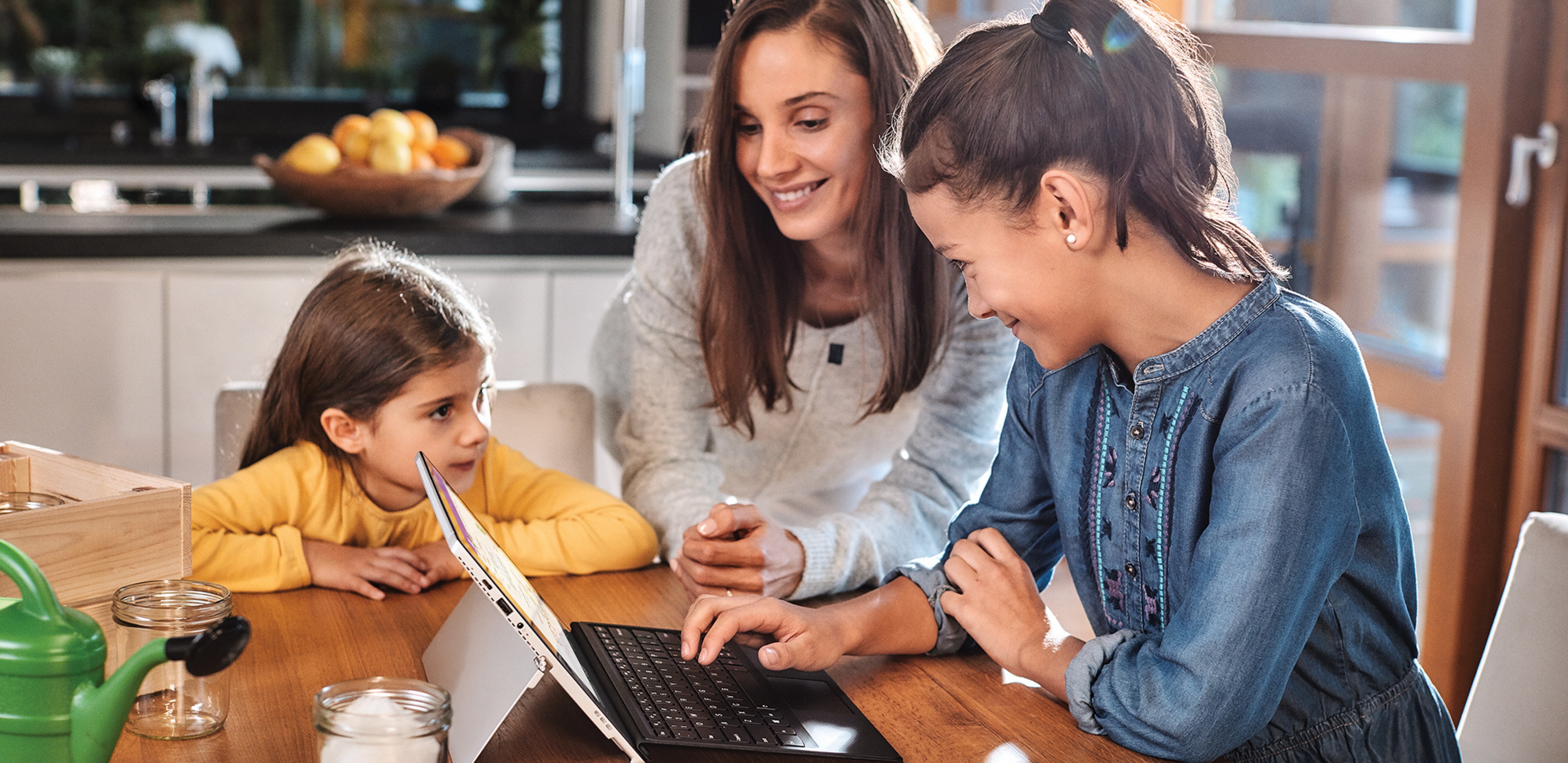 Woman sitting at table with two little girls working on a PC.