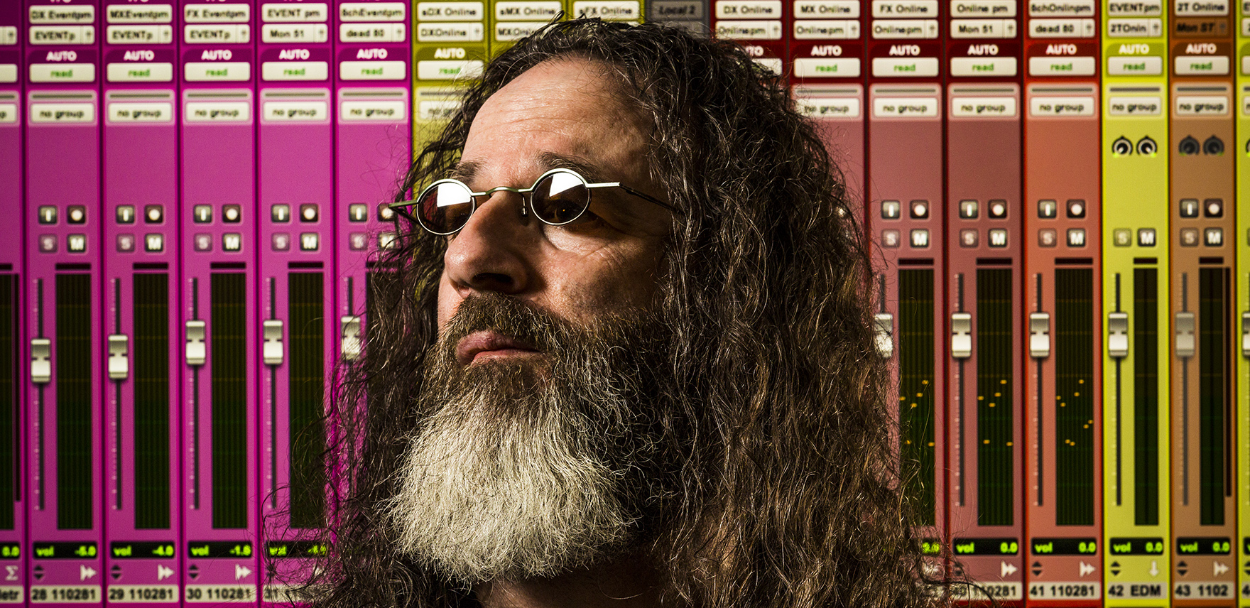 Man with a beard wearing sunglasses in front of colorful sound equipment