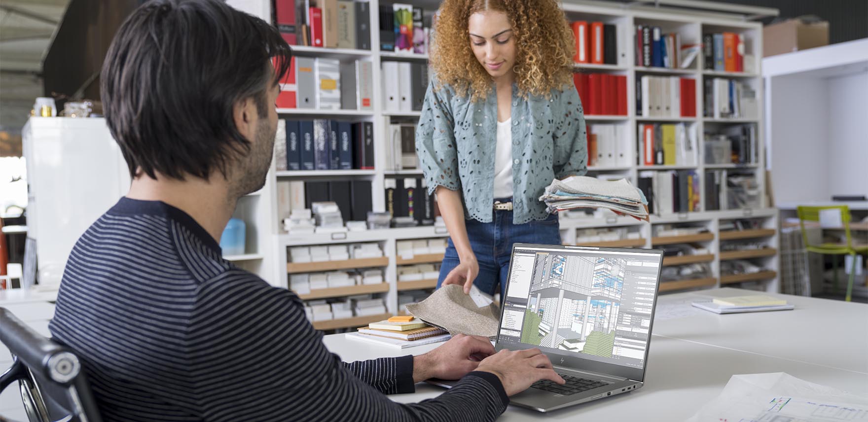 A man at a table works on a HP ZBook Studio while a woman stands on the other side of the table