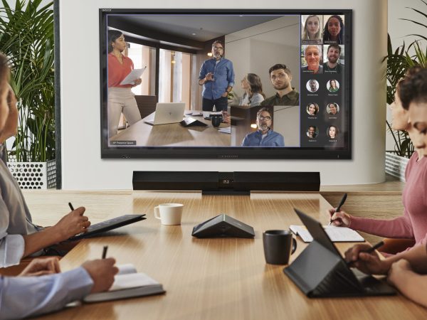 Three people sitting at a table working while talking to another group on a monitor
