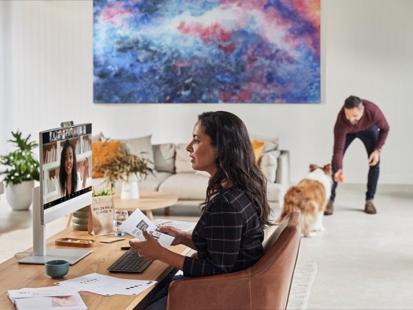 Woman sitting at a table in living room on a video chat with man in background playing with dog