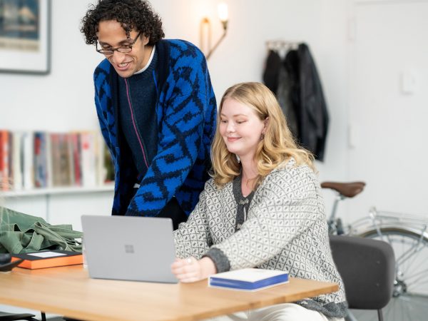Teacher looking over a student's shoulder at what's on her laptop device