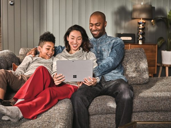Family of three -- man, woman and boy -- sitting on a couch looking at a Surface device