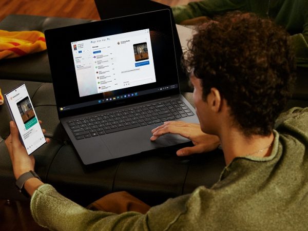 Person holding mobile phone in one hand and working on laptop with the other