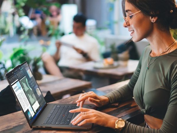Woman sitting at an outdoor cafe working on a laptop, smiling