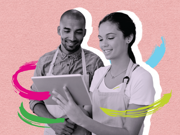 Man and woman wearing aprons smile as they interact with a tablet device