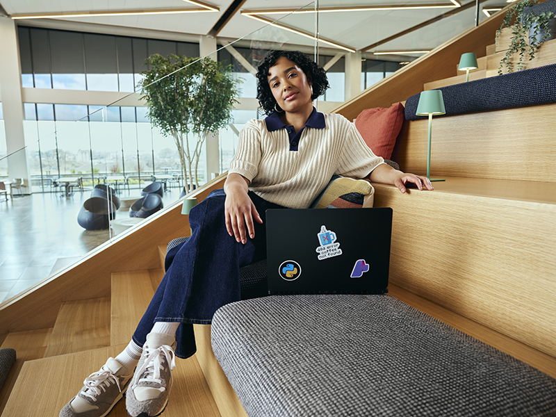 Woman with a laptop sitting on wooden steps in an open space.