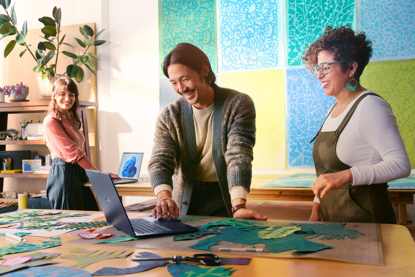 Three people smiling as they work on laptop computers in a creative studio.