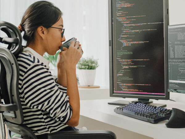 Woman sipping from a cup as she sits at a computer workstation.