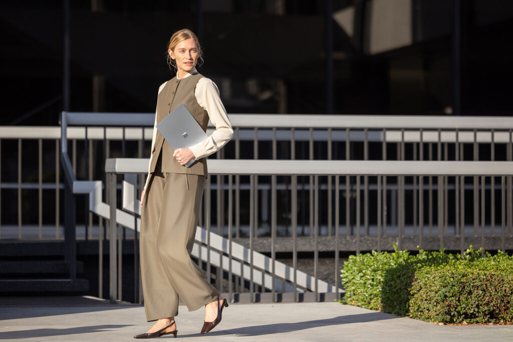 Woman in a business suit walking outside, carrying her Surface Laptop.