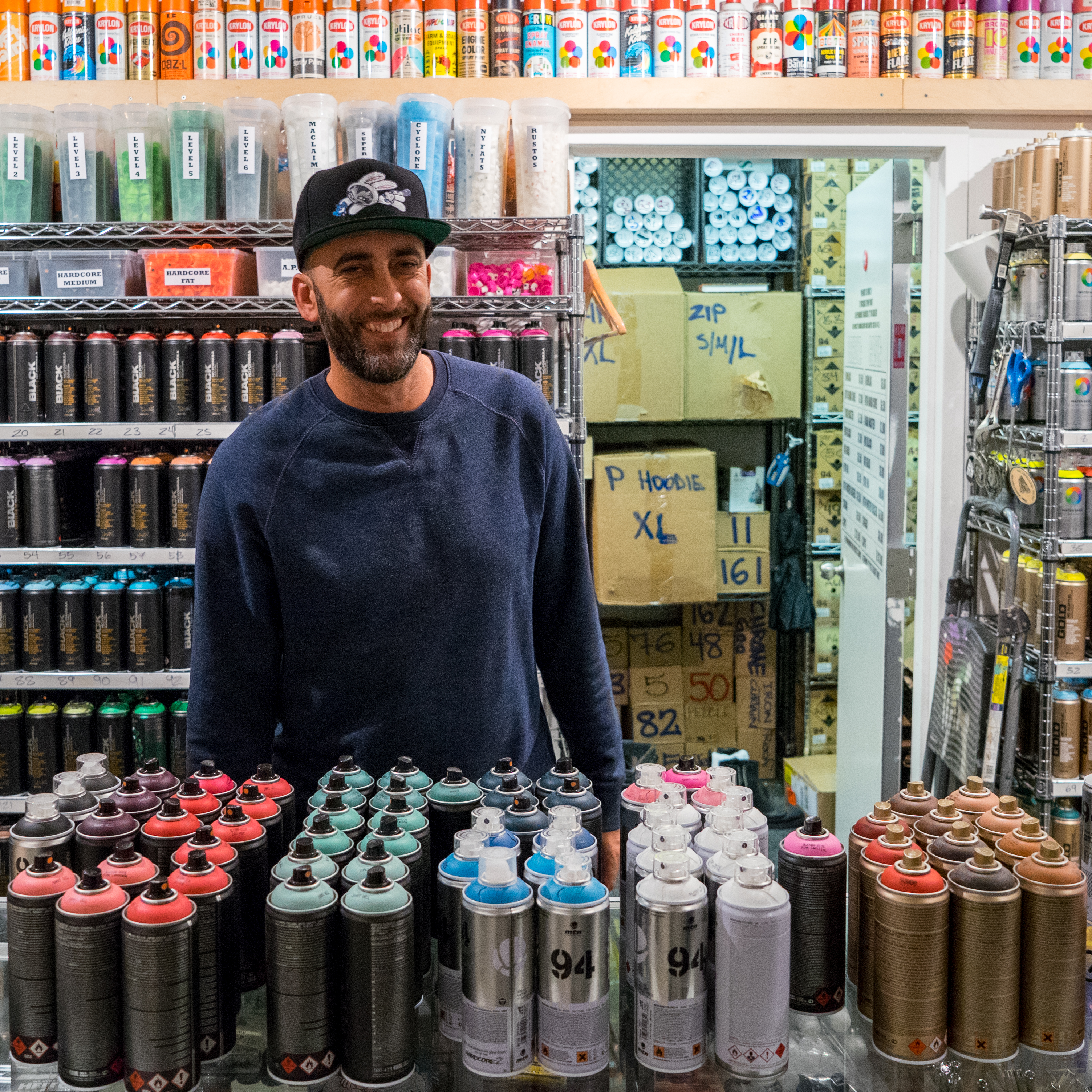 Dave Ross standing in front of spray+paint cans he used to create his mural.