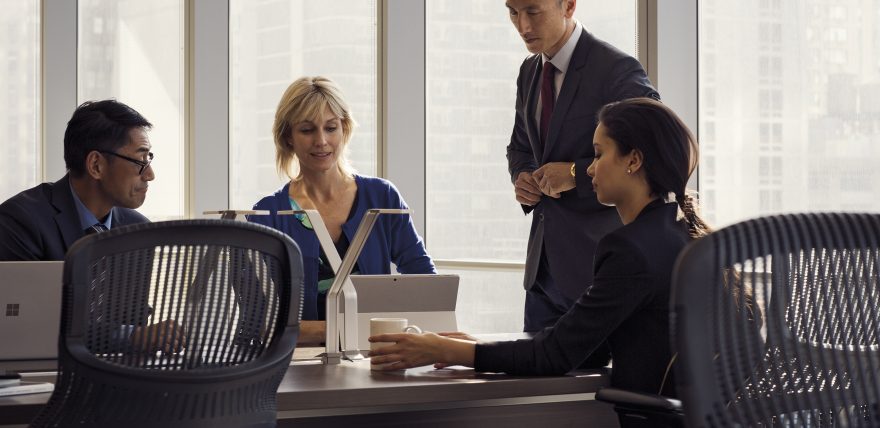 Men and woman sitting around a conference table looking at a Surface Pro.