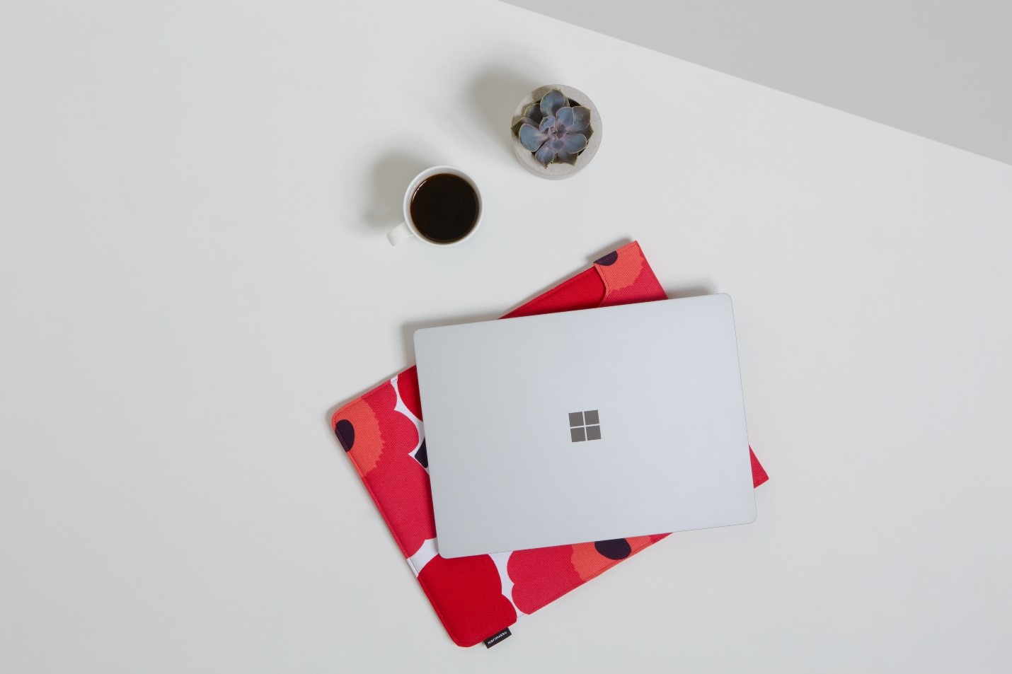 Surface Laptop on a table with a Marimekko sleeve, next to it is a plant and a cup of coffee.