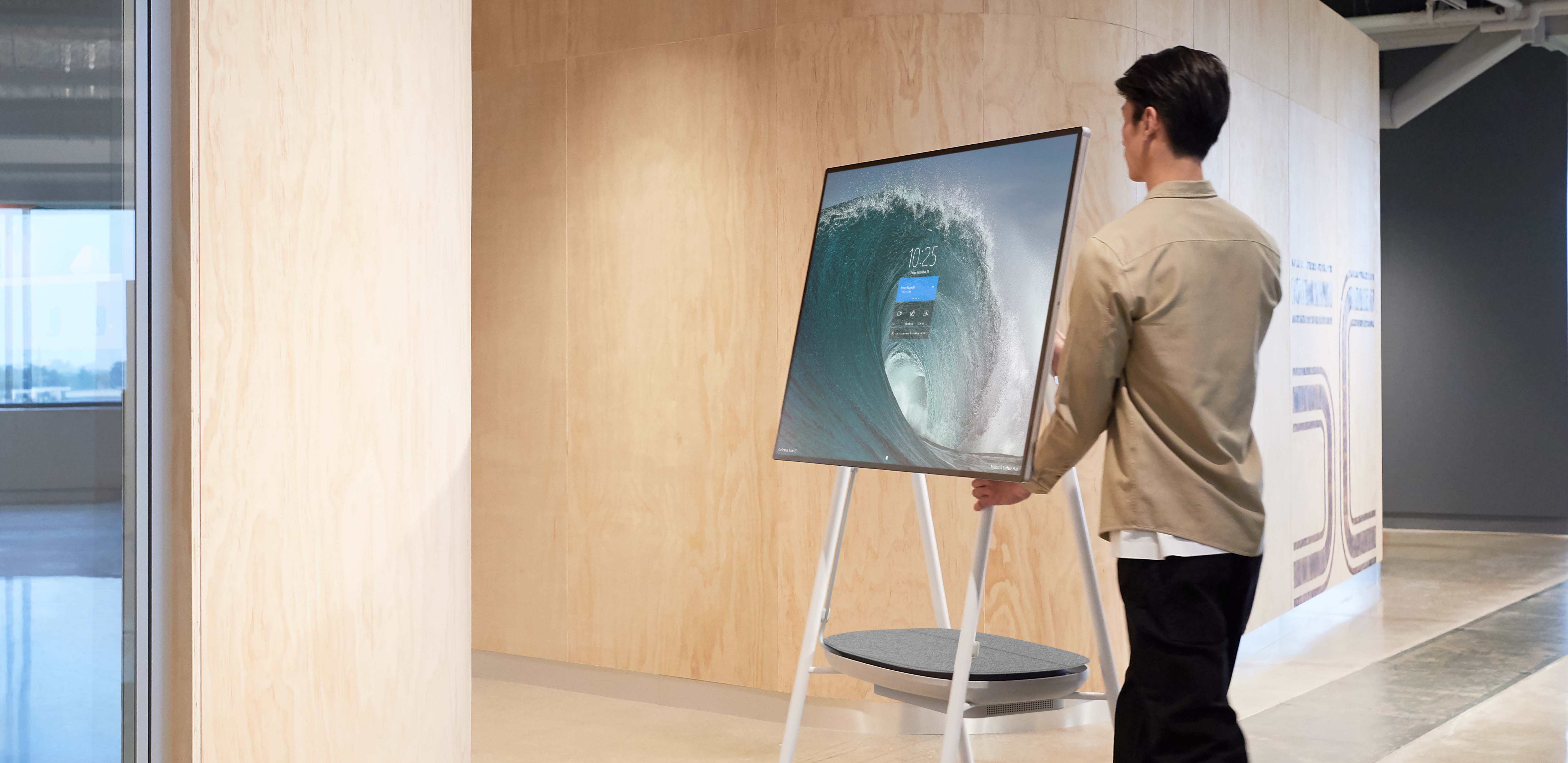 Man wheels a Surface Hub 2S into a meeting room