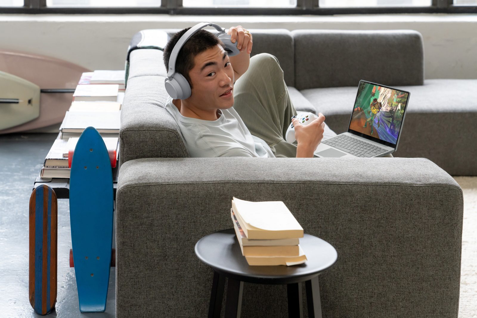 a person has a headset on and holds game controller, with a laptop device on his knee