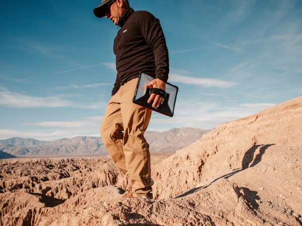 Man walking through a desert with a tablet device connected to his left hand with a strap